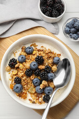 Bowl of healthy muesli served with berries on white wooden table, flat lay