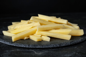Cut raw potatoes on black table, closeup