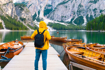 Inspiring traveler in yellow jacket visited popular lake Braies with wooden boats and the cinematic beautiful mountains of Dolomites Alps in autumn 