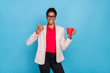 Photo of positive person hold coffee mug demonstrate thumb up isolated on blue color background