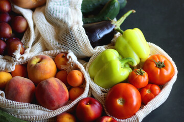 Reusable mesh bags for fruits and vegetables, filled with various healthy food. Dark background, selective focus.