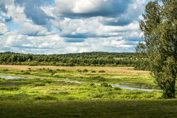 Fototapeta na wymiar Background of a blue sky with clouds, a green field, river and forest