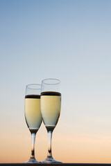 Two champagne glasses filled with champagne are lined up against the evening sky.