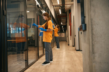 Two employees cleaning company clean the mirrored partitions coworking space
