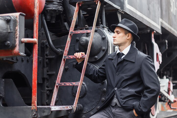 Men's photo session in a classic plaid suit and hat against the backdrop of an old steam locomotive.