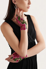 Cropped shot of a lady in a black dress and short floral fingerless gloves against the light wall. The elegant fingerless gloves are made out of the openwork fabric with embroidered flower pattern.