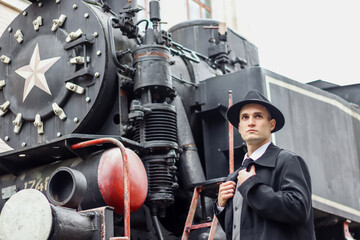 Men's photo session in a classic plaid suit and hat against the backdrop of an old steam locomotive.