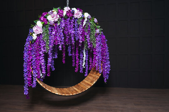 round swing with purple flowers against a dark wall. wedding iron swing with a wooden seat in a photo studio. wedding photo zone with indoor swing
