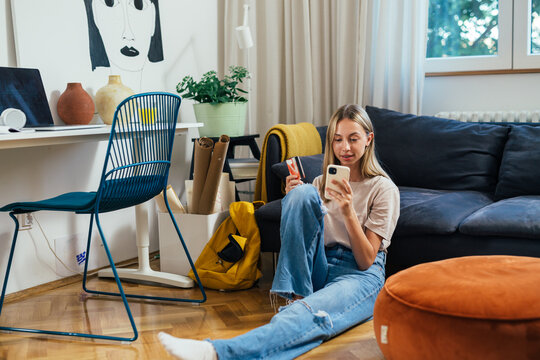 european teenager female shopping online using her mobile phone while sitting in her room