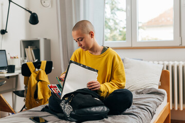 young shave head female packing school bag in her room