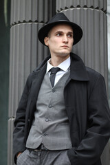 Men's photo session in a classic checkered suit and hat against the backdrop of columns.