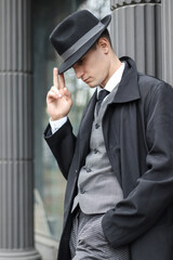 Men's photo session in a classic checkered suit and hat against the backdrop of columns.