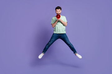 Fototapeta na wymiar Full length photo of nice young man jumping high hold megaphone shouting dressed stylish gray garment isolated on purple color background