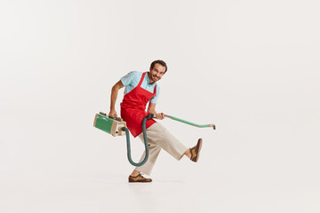 Portrait of cheerfulman in apron vacuumingand daning isolated over white background