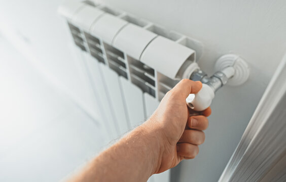 Male hand adjusting thermostat to turn on the radiator heater at home.