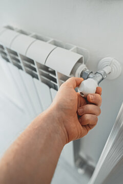 Male hand adjusting thermostat to turn on the radiator heater at home.