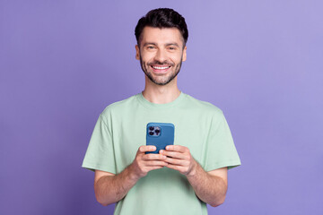 Photo portrait of attractive young man holding device toothy beaming smile dressed stylish gray clothes isolated on purple color background
