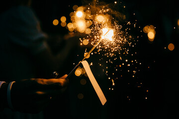 Bright festive sparkler in hand. Burning sparkle in darkness. Unrecognizable person holding glowing holiday sparkling hand fireworks, shining fire flame. Bengal fire against black background