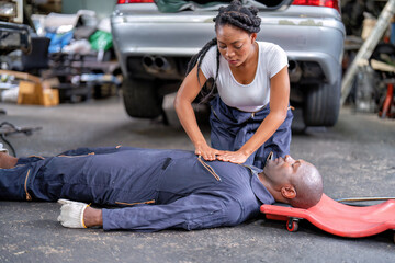 Mechanical guy at car repair shop got accident lay on the floor mechanical girl first aid life saving by perform cardiopulmonary resuscitation CPR before the medic come