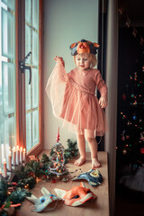 Cute little girl is dressing up a tiny Christmas tree and trying on New Year's animal masks. Image with selective focus and toning. 