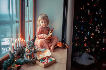 Cute little girl is dressing up a tiny Christmas tree and trying on New Year's animal masks. Image with selective focus and toning. 
