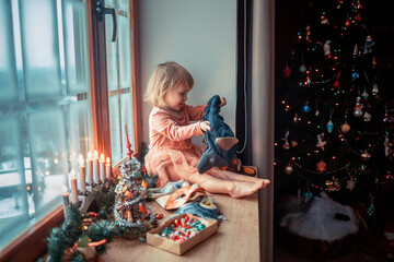 Cute little girl is dressing up a tiny Christmas tree and trying on New Year's animal masks. Image...