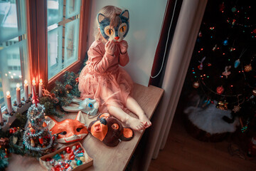 Cute little girl is dressing up a tiny Christmas tree and trying on New Year's animal masks. Image with selective focus and toning. 