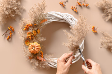 Woman making wreath with orange flowers and dry natural materials over beige background. Top view....