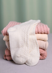 Warm white wool socks are lying on a stack of knitted things. Vertical photo.