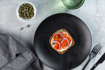 open sanwiches with dark rye bread, salmon, pickled capers, red onion,black background, top view.