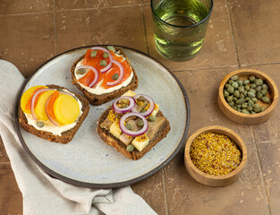 assorted toasts with dark rye bread, herrings, smoked salmon and capers on wood background