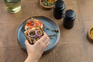 kid hand pick up toast with dark rye bread, herrings, smoked salmon and capers. copy space. Vertical
