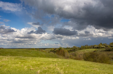 Spring landscape, dramatic sky over green hills before rain. The sun through the clouds illuminates the green meadows and ravines.