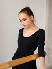 Portrait of female dancer in black outfit leaning at wooden handrail and looking down while training in a dance studio - 541452429