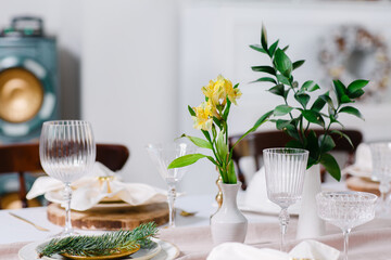 Fresh flowers among the cutlery and dishes, stylish table setting on Christmas Eve for the whole family.