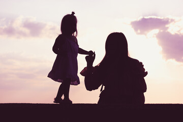 A mom, mother holding by the hand a little daughter against a pink sky. Two contrasting figures silhouettes. Interaction of parents children. Psychology of parenting a child, kid. Reproductive Clinic. - obrazy, fototapety, plakaty