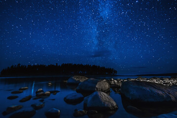 night landscape with a starry sky over sea water with stones and forest. Astrophotography with many...