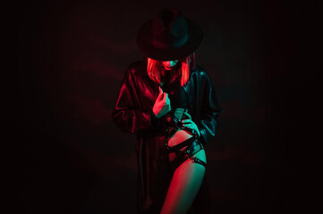Sexy girl in beautiful underwear, leather belt and hat poses beautifully with neon colored light on a black background