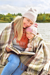 Mom and daughter are reading a book on a bench. Mother and daughter on a walk. Autumn season. Sunny day. Happy family outdoors - 541461080