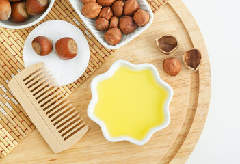 Hazelnut oil in a small white bowl and wooden hairbrush. Homemade face or hair mask, facial cleanser, natural beauty treatment and spa recipe. Top view, copy space.