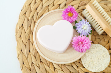 Fototapeta na wymiar Heart shaped bar of soap (facial cleanser, solid shampoo) and purple flowers. Natural beauty treatment and skin care concept. Top view, copy space.