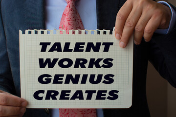 The paper in the hand of the man in the suit reads ''talent, works, genius, creates ''.