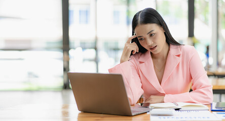 Obraz premium Asian businesswoman analyzing a report pointing to a graph with a pen, laptop and calculator. In workstation accountant telemarketing concept, ecommerce, free online marketing.