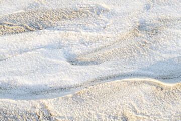 Pattern of snow covered ripples in the sand on the beach, lit by the low sun during winter.