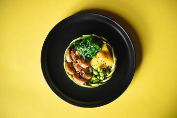 Appetizing bowl with shrimps and vegetables sprinkled with sesame seeds on a yellow background