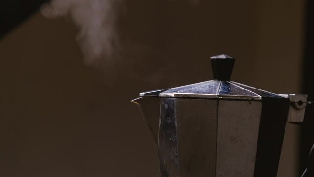 Hot coffee is boiling and steam comes out of a moka pot, close-up. Coffee boils in geyser coffee maker kettle on grey background. Making delicious coffe with a moka pot.