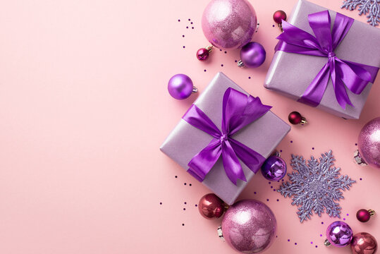 New Year atmosphere concept. Top view photo of lilac present boxes with bows pink violet baubles snowflake ornaments and shiny sequins on isolated pastel pink background with empty space