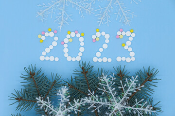 White medical pills in form of number 2023, Christmas tree and snowflakes on blue background....