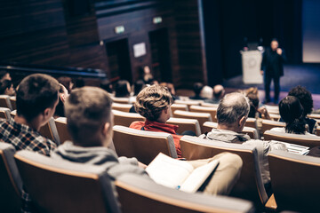 Speaker giving a talk in conference hall at business event. Rear view of unrecognizable people in audience at the conference hall. Business and entrepreneurship concept.