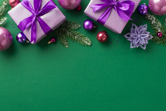 Christmas Eve concept. Top view photo of lilac present boxes with purple ribbon bows pink violet baubles flower ornament fir branches in frost and sequins on isolated green background with empty space